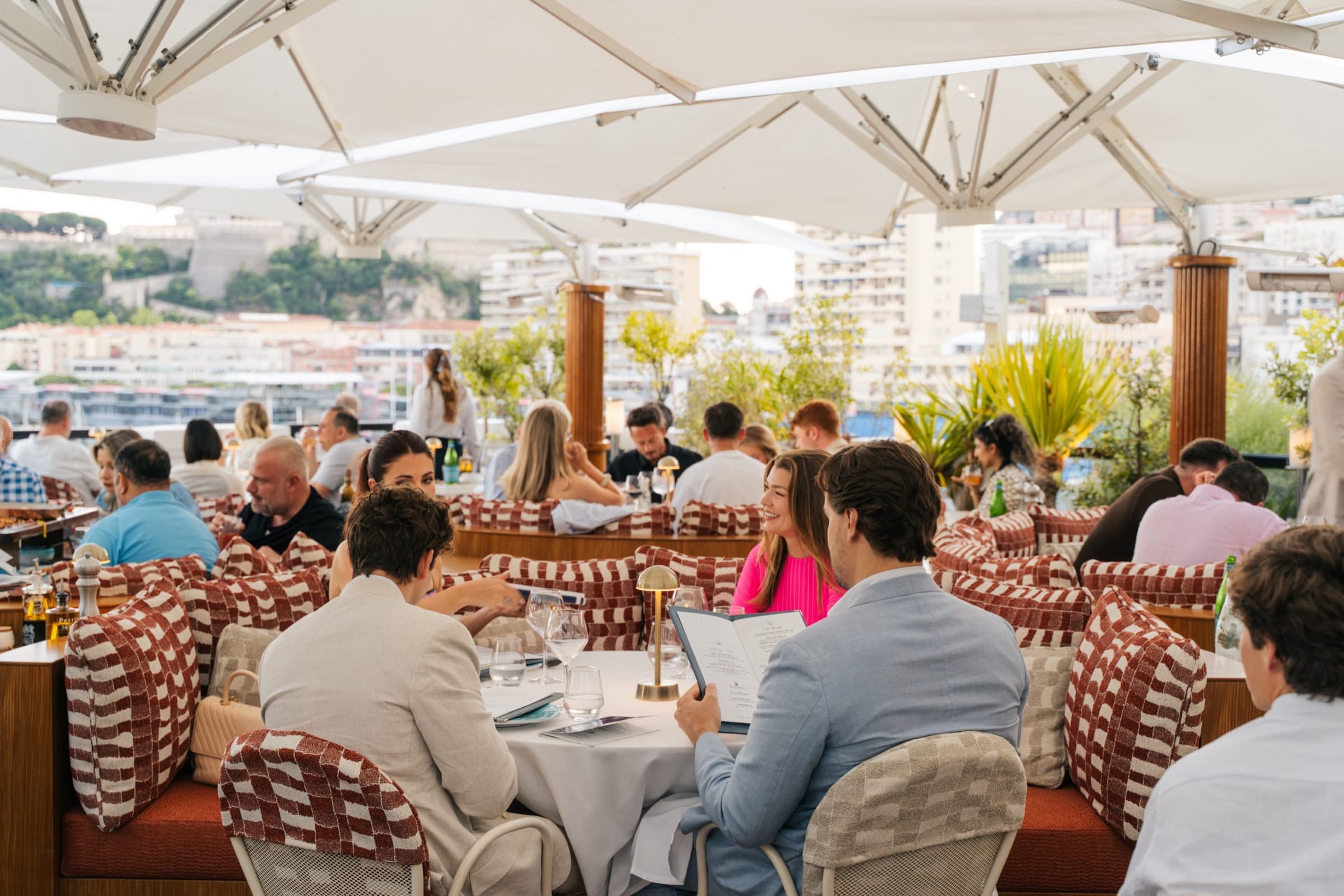 La Môme Monaco's rooftop under parasols, the port below